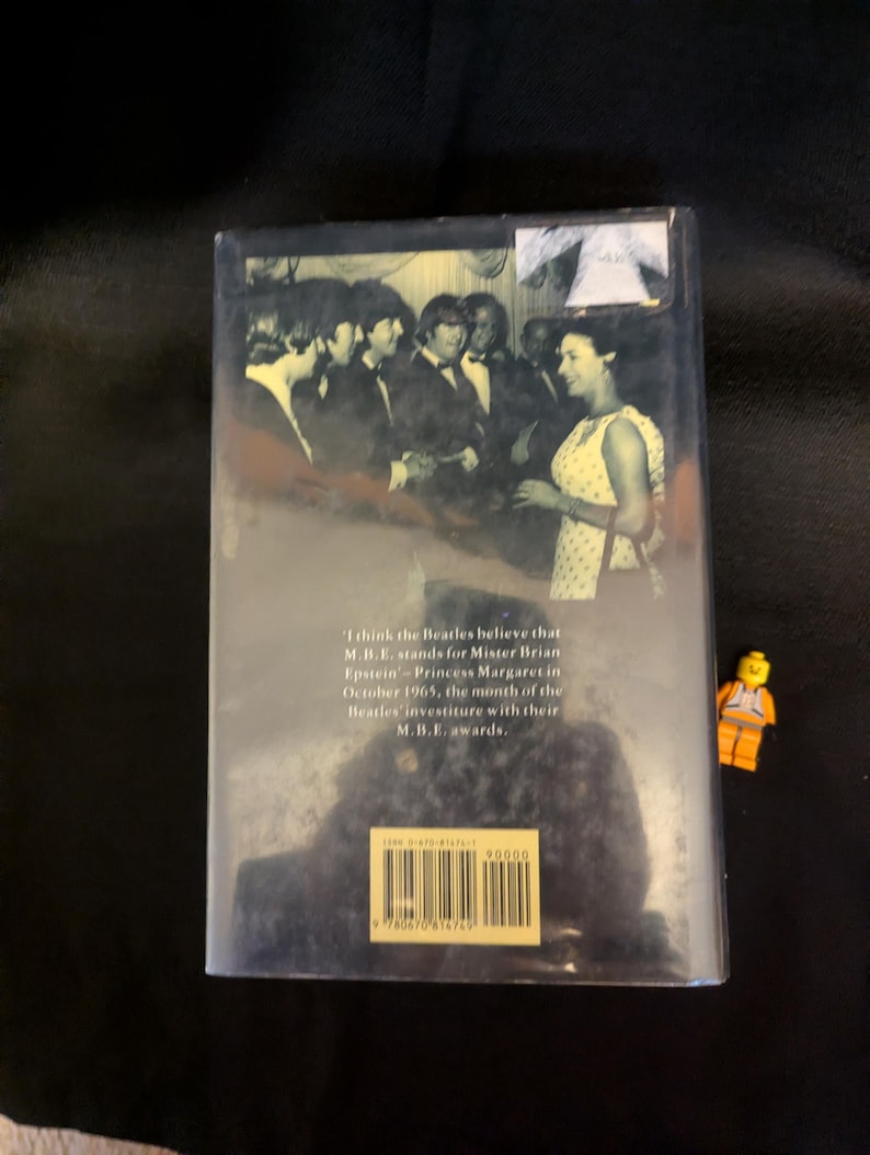 Puede incluir: Portada de libro con una foto en blanco y negro de The Beatles y una mujer. El texto dice: "Creo que los Beatles creen que M.B.E. significa Mister Brian Epstein - Princesa Margarita en octubre de 1965, el mes de la investidura de los Beatles con sus premios M.B.E."
