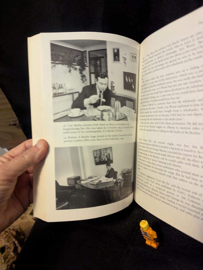 Puede incluir: Un libro abierto con fotograf&iacute;as en blanco y negro. Una foto muestra a un hombre comiendo en una mesa, la otra a un hombre en un escritorio. Una peque&ntilde;a figura de Lego est&aacute; en primer plano.