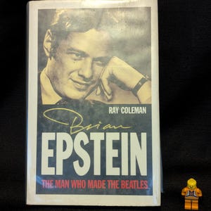 Puede incluir: Portada de libro con un retrato sepia de un hombre, el t&iacute;tulo "Brian Epstein" en blanco y el subt&iacute;tulo "The Man Who Made The Beatles". Tambi&eacute;n es visible el nombre del autor, Ray Coleman. Una peque&ntilde;a figura de Lego est&aacute; en primer plano.