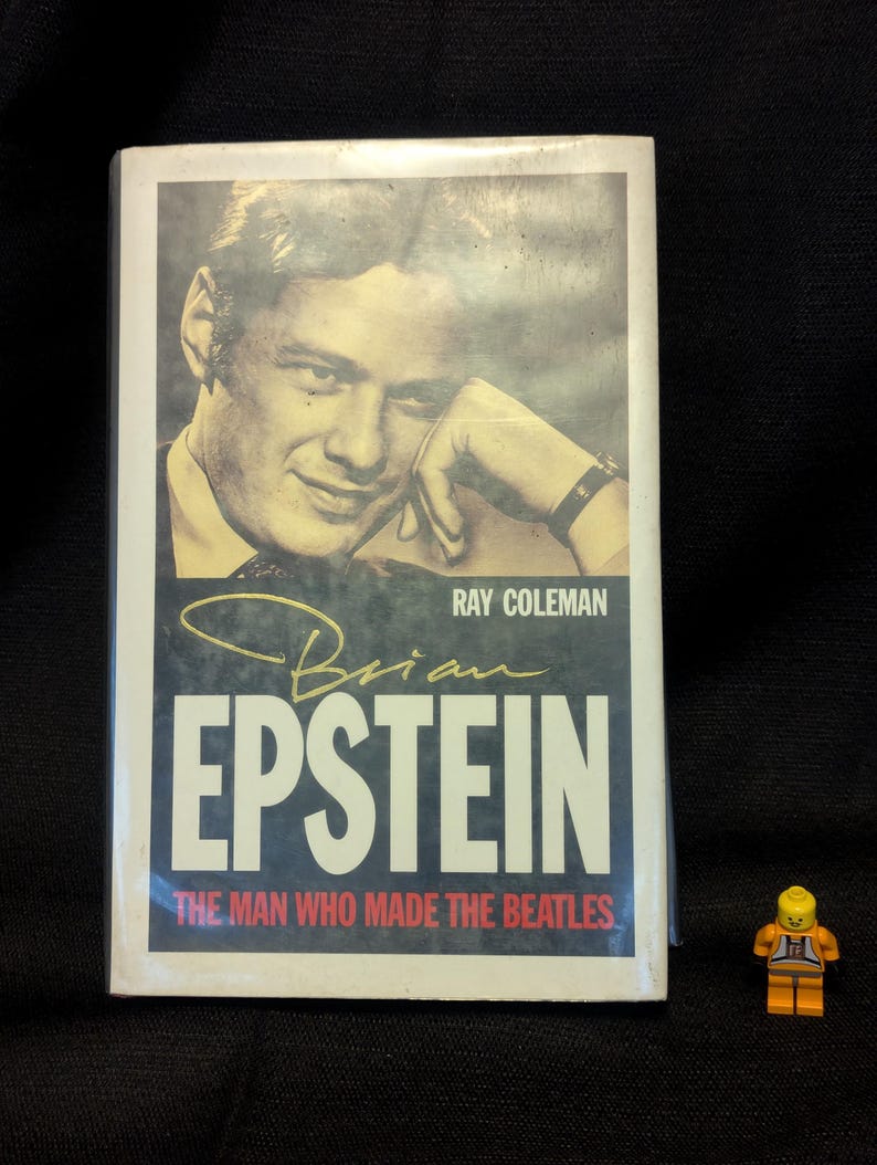 Puede incluir: Portada de libro con un retrato sepia de un hombre, el t&iacute;tulo "Brian Epstein" en blanco y el subt&iacute;tulo "The Man Who Made The Beatles". Tambi&eacute;n es visible el nombre del autor, Ray Coleman. Una peque&ntilde;a figura de Lego est&aacute; en primer plano.