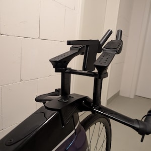 May include: A black bicycle cockpit featuring aerodynamic handlebars with integrated armrests and a central mounting bracket. The frame is dark purple and black with the text I'm OK printed on the side. The setup includes a stem and extensions.