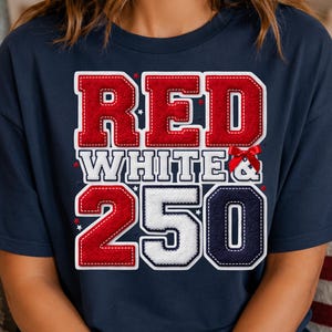 Könnte beinhalten: Ein dunkelblaues T-Shirt mit kurzen Ärmeln und einem großen Grafikdruck mit dem Text RED WHITE & 250. Die Buchstaben und Zahlen haben eine texturierte, gestickte Optik in Rot, Weiß und Dunkelblau, akzentuiert durch eine kleine rote Schleife.