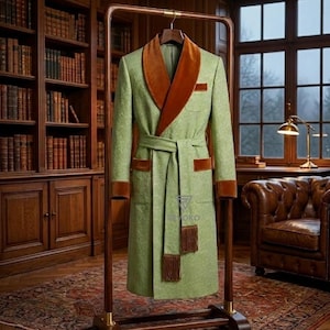 May include: A green robe with brown velvet trim and a matching belt hangs on a wooden rack. The robe features a shawl collar, pocket trim, and sleeve cuffs in a contrasting brown color. The robe has a textured pattern.