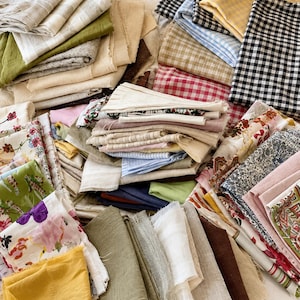 Puede incluir: Una gran colección de retales de tela variados en diversos colores, texturas y estampados. El montón incluye tonos neutros sólidos, verdes tierra, amarillo mostaza, cuadros vichy en negro, azul y rojo, y estampados florales con bordes deshilachados.