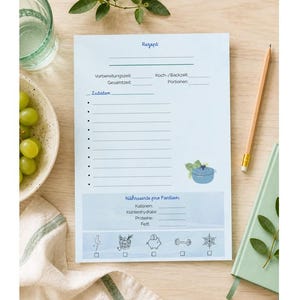 Könnte beinhalten: Ein hellblaues Rezeptnotizbuch mit dem Wort "Rezept" oben. Das Notizbuch hat Linien für Zutaten und Nährwertangaben. Ein Bleistift und ein grünes Notizbuch befinden sich neben dem Notizbuch. Eine Schüssel mit grünen Trauben und ein Glas Wasser sind ebenfalls im Bild.