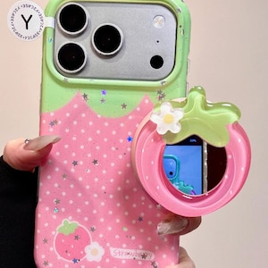May include: A green and pink phone case with a strawberry design. The case has a glittery finish and a strawberry-shaped grip. The word "Strawberry" is printed on the case.