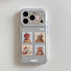 May include: A clear smartphone case featuring a camera lens frame with small icons and the text "yummy". The back displays four square images of teddy bears and rabbits on a checkered background, accented with scattered pastel-coloured stars.