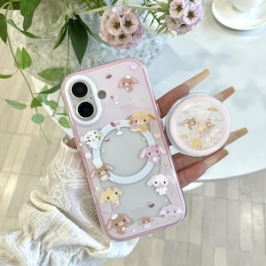 May include: A clear phone case with a light pink border featuring various cartoon dog illustrations, small hearts, and a circular magnetic ring. A matching circular phone grip with a clear top filled with small floating dog-shaped confetti pieces.