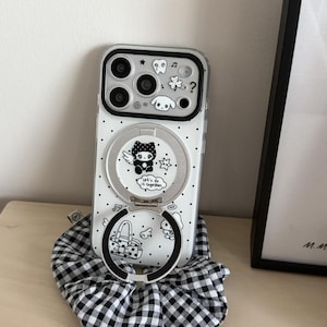 May include: A clear phone case with a black border and a white polka dot pattern. The back features black and white illustrations of a tooth, a clover, a dog, and a character with wings. A circular metal ring stand displays the text Let's do it together.
