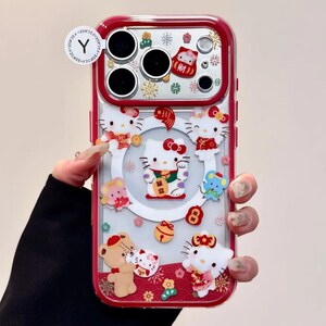 May include: A clear phone case with a red border, featuring multiple Hello Kitty figures and other decorative elements. The case has a festive design with a central Hello Kitty figure holding a gold ingot. The case has a Y2CASE sticker.