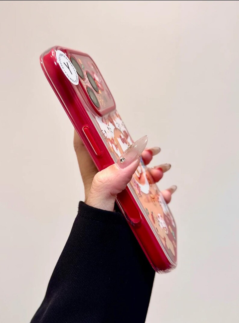 May include: A red phone case with a clear back featuring a cartoon design. The case has a glossy finish and a raised edge for screen protection. The design includes various cartoon characters in shades of brown, white, and red.