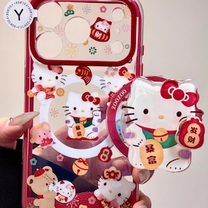 May include: Clear phone case with a red border featuring Hello Kitty characters in various poses. The case has a transparent design with decorative elements and text in Chinese characters.