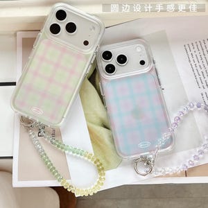 Puede incluir: Dos fundas transparentes para smartphone con un patrón de cuadros de enfoque suave. La funda izquierda presenta una cuadrícula rosa y verde, mientras que la derecha tiene una azul y morada. Cada funda incluye una correa de cuentas a juego.