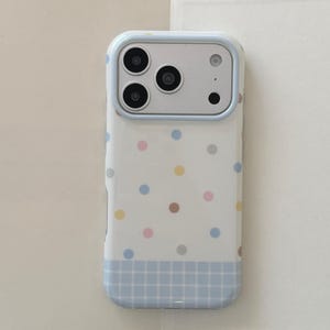 May include: A white smartphone case featuring a pattern of small, multicoloured polka dots in shades of blue, pink, yellow, and brown. The bottom section of the case has a light blue grid pattern, and the camera cutout is framed in light blue.