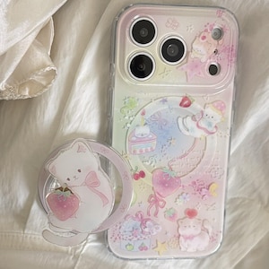 May include: A clear smartphone case with a pastel gradient background featuring illustrations of white kittens, pink strawberries, cakes, and bows. A circular phone grip with a white kitten holding a pink strawberry is attached to the side.