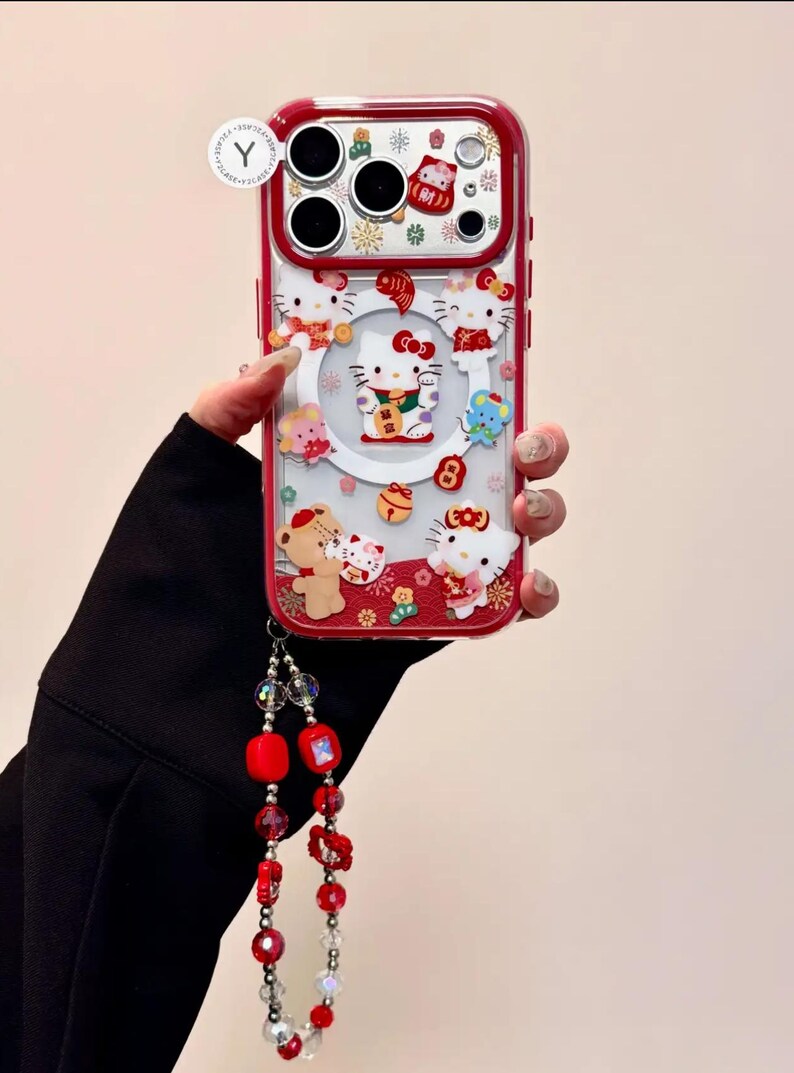May include: A red and clear phone case featuring Hello Kitty and other cartoon characters. The case has a red border and a decorative wrist strap with red beads. The design includes festive elements.