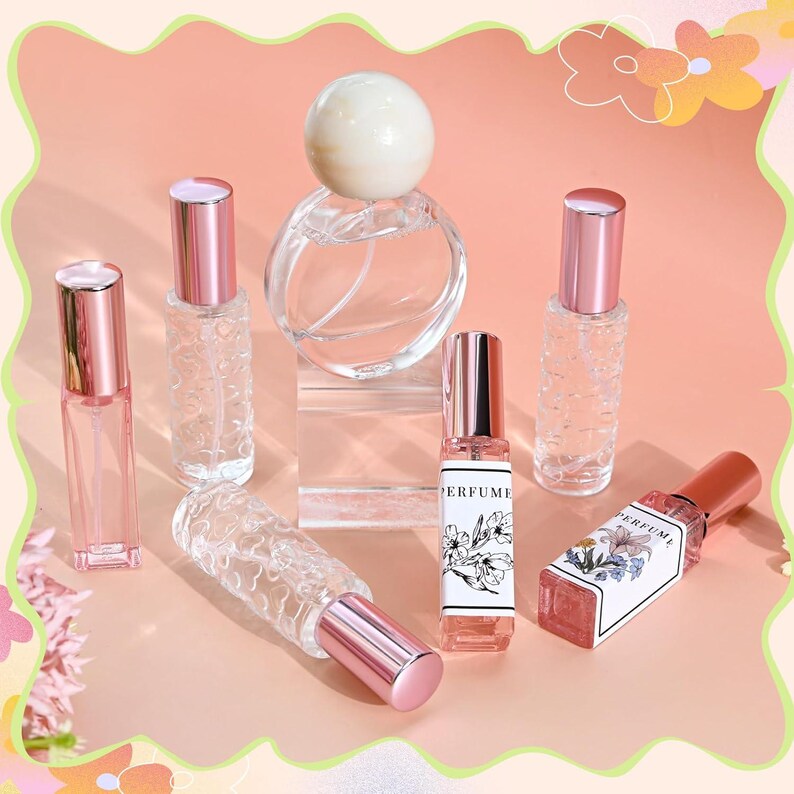 May include: A collection of clear glass perfume bottles with metallic pink caps. One round bottle features a white spherical topper, while several rectangular bottles have textured surfaces. Two bottles display white labels with floral illustrations and the text PERFUME.