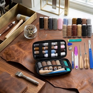 May include: A leathercrafting kit with various tools and supplies. The image shows spools of thread in multiple colors, needles, a measuring tape, and a variety of leatherworking tools, including awls and a mallet. The items are arranged on a brown leather surface.