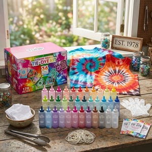 May include: A tie-dye kit with 36 unique colours, a box with the text "COLOR MANIA TIE-DYE KIT", and two tie-dye shirts. The kit includes bottles of dye, rubber bands, gloves, and instructions. The shirts are blue, orange, and red.