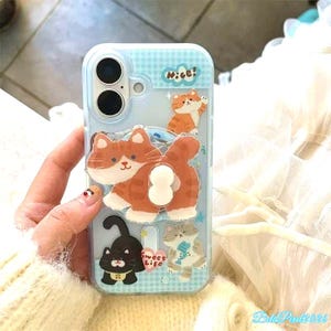 May include: A light blue phone case with a cartoon cat design. The case features multiple cat illustrations in orange, black, and gray, with the word "Nice!" printed on the top. The case is designed to fit a smartphone.
