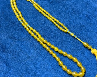 May include: A long string of translucent yellow prayer beads featuring small turquoise accent beads interspersed throughout the strand. The prayer beads terminate in a larger yellow bead and a yellow tassel at the end of the cord.