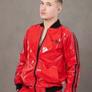 May include: A glossy red bomber jacket with a black collar, black cuffs, and black stripes running down the sleeves. The jacket features a front zipper closure and the text PVCUP printed in black on the left chest area of the shiny red material.