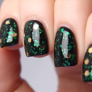 May include: Close-up of manicured nails with a black base and green and gold glitter. The nails are oval-shaped and glossy. The text "spellboundnails.blogspot.com" is visible on the image.