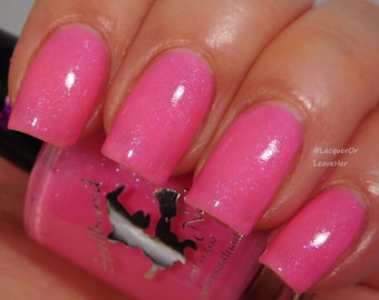 May include: Pink nail polish with a shimmer finish. The bottle is labeled "Spellbound" and has a small illustration of a witch on a broom. The polish is shown on four fingernails.