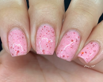 May include: Close-up of four fingernails painted with a pink nail polish with red glitter. The nail polish has a textured, bumpy finish.