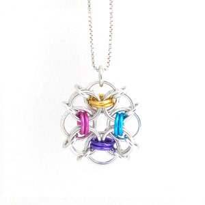Puede incluir: Un collar de cadena de plata con un colgante de malla de cadena de plata y multicolor. El colgante es de dise&ntilde;o circular con cuatro anillos de malla de cadena de plata y cuatro anillos de malla de cadena de color. Los anillos de color son dorado, rosa, azul y morado.