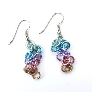 May include: A pair of silver dangle earrings with a gradient of blue, purple, and pink metal rings.