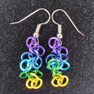 May include: A pair of colourful handmade earrings. The earrings are made from linked metal rings in a rainbow of colours: purple, blue, green, and yellow. They have silver-tone ear wires. A unique and eye-catching accessory.