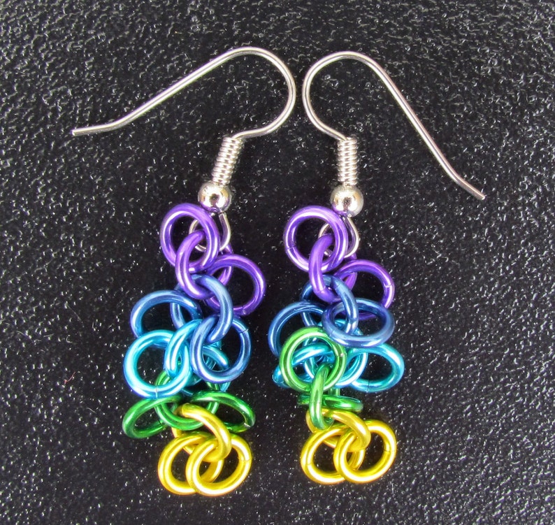 May include: A pair of colourful handmade earrings. The earrings are made from linked metal rings in a rainbow of colours: purple, blue, green, and yellow. They have silver-tone ear wires. A unique and eye-catching accessory.