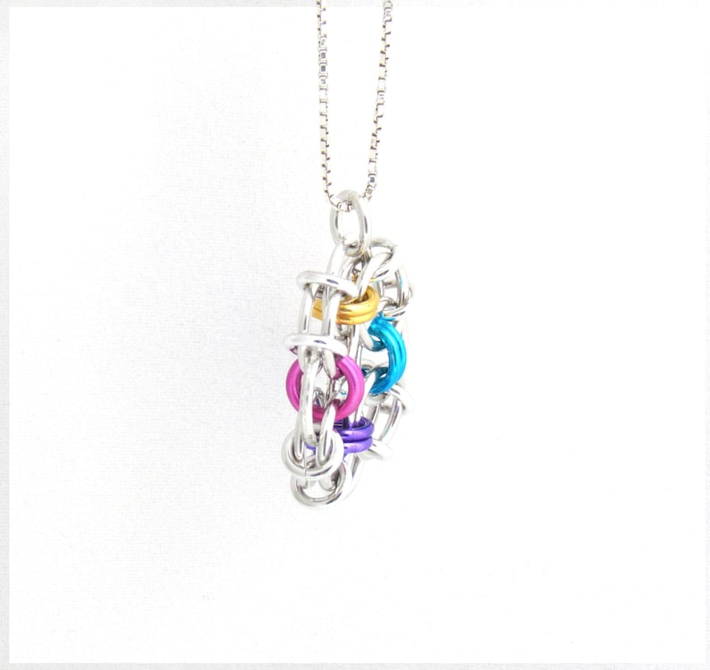 Puede incluir: Un collar de cadena de plata con un colgante colorido hecho de anillos de metal interconectados. El colgante presenta anillos en tonos de azul, rosa, morado y dorado.