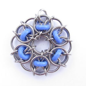 Puede incluir: Un colgante de malla de cadena plateada con un diseño de flor y cuentas azules.
