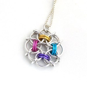 Puede incluir: Un collar de cadena de plata con un colgante colorido. El colgante est&aacute; hecho de anillos de metal interconectados en plata, oro, morado, rosa y azul.