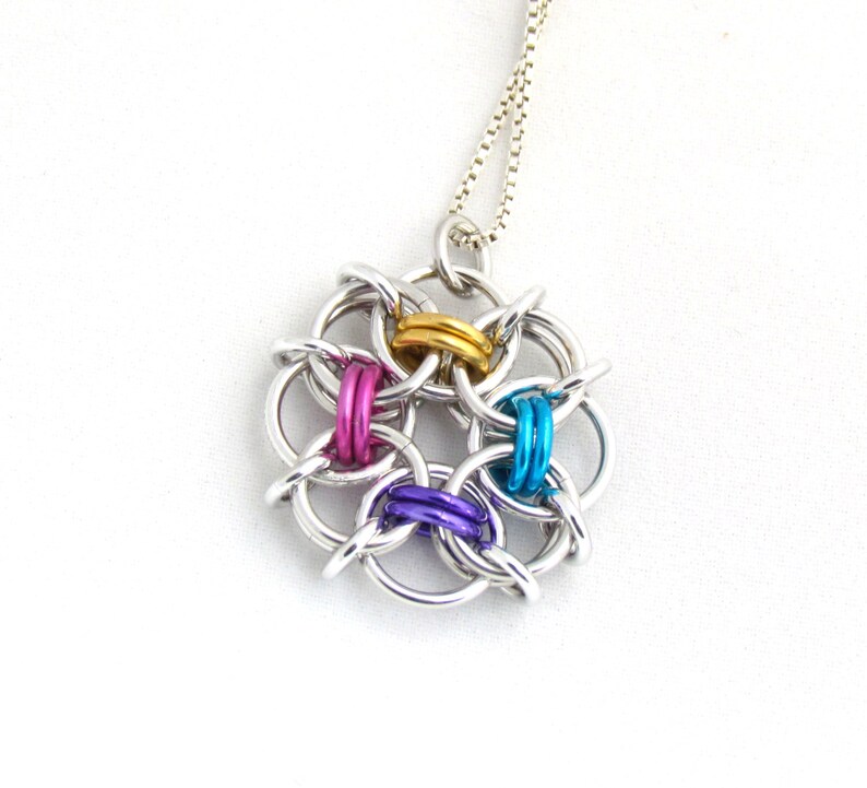 Puede incluir: Un collar de cadena de plata con un colgante colorido. El colgante est&aacute; hecho de anillos de metal interconectados en plata, oro, morado, rosa y azul.