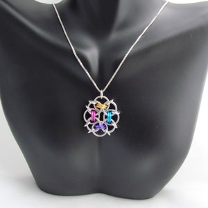 Puede incluir: Un collar de cadena de plata con un colgante colorido. El colgante est&aacute; hecho de anillos de plata con acentos dorados, azules, rosados y morados.