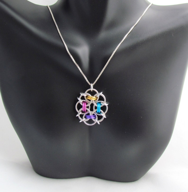 Puede incluir: Un collar de cadena de plata con un colgante colorido. El colgante est&aacute; hecho de anillos de plata con acentos dorados, azules, rosados y morados.