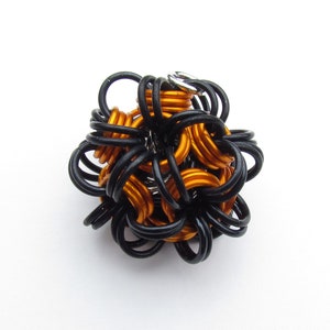 Puede incluir: Una escultura de alambre negro y naranja en forma de esfera. La escultura está hecha de muchos pequeños bucles de alambre interconectados.