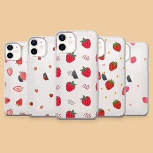 May include: A collection of clear phone cases with a strawberry pattern. The cases feature a repeating design of red strawberries with green leaves, some with black seeds, and wavy lines on a white background. Some cases have daisy and heart patterns.