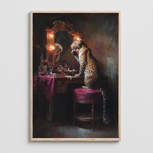 May include: A framed artwork depicts a leopard seated at a vanity table, applying makeup in a mirror. The scene is richly detailed with a dark, moody color palette, featuring a burgundy stool and table cloth. The leopard's spotted coat contrasts with the ornate gold mirror frame.
