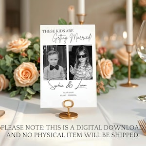 Puede incluir: Una tarjeta de mesa de boda blanca con el texto "THESE KIDS ARE Getting Married!" y dos fotos en blanco y negro. La tarjeta dice "Sophia & Liam" y la fecha "05.08.2026 Miami, Florida". La tarjeta est&aacute; sujeta por un soporte de metal dorado.