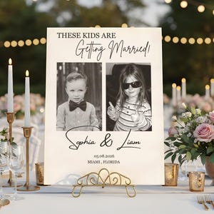 Puede incluir: Un letrero de boda con el texto "THESE KIDS ARE Getting Married!". Presenta dos fotos en blanco y negro de ni&ntilde;os. El letrero incluye los nombres "Sophia & Liam" y la fecha 05.08.2026, Miami, Florida. El letrero se muestra en un soporte dorado.