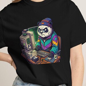Puede incluir: Una camiseta negra con un gráfico de un panda que lleva un gorro y una chaqueta colorida, sentado en un escritorio con una computadora antigua, teclado y ratón. El panda tiene una expresión concentrada mientras usa el equipo.