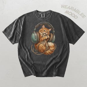 May include: A charcoal gray short-sleeve t-shirt featuring a graphic of an orange tabby cat wearing large teal headphones and playing with a tangled black cord. The text WEARABLE MOOD is printed in the upper right corner of the garment.