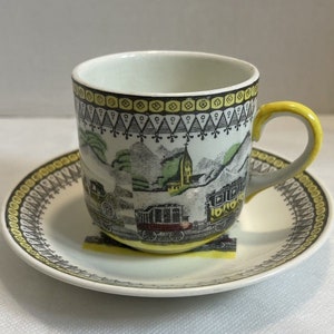 以下が含まれることがあります： 黒と白の列車のシーンと黄色のアクセントが施されたヴィンテージのティーカップとソーサーのセット。カップにはハンドルがあり、ソーサーには波状の縁があります。