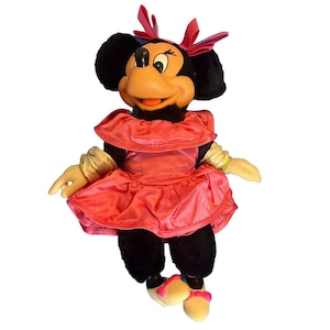 Puede incluir: Mu&ntilde;eca de peluche de Minnie Mouse, con cabeza y cuerpo negros, cara color melocot&oacute;n y vestido rosa brillante. La mu&ntilde;eca tiene un lazo y zapatos rosas a juego, con guantes amarillos. Un personaje cl&aacute;sico de Disney.