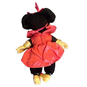Puede incluir: Mu&ntilde;eca de peluche vintage de Minnie Mouse, vista desde atr&aacute;s, con un vestido rojo con un gorro a juego y guantes dorados. La mu&ntilde;eca tiene pelo negro y zapatos amarillos. Un personaje cl&aacute;sico de Disney.