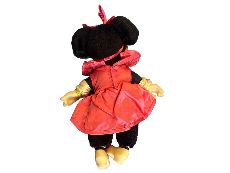 Puede incluir: Mu&ntilde;eca de peluche vintage de Minnie Mouse, vista desde atr&aacute;s, con un vestido rojo con un gorro a juego y guantes dorados. La mu&ntilde;eca tiene pelo negro y zapatos amarillos. Un personaje cl&aacute;sico de Disney.